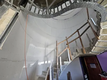Curved drywall wall rising alongside a stairwell under a framed ceiling ring