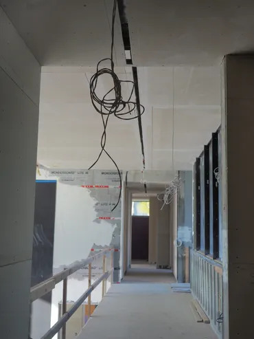 Drywall corridor with a ceiling bulkhead and exposed wiring before finishing