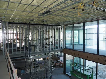 Metal stud framing and ceiling grid in a double-height room with glass walls