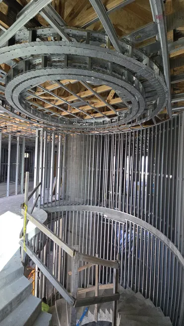 Circular metal framing ring above a stairwell lined with vertical studs